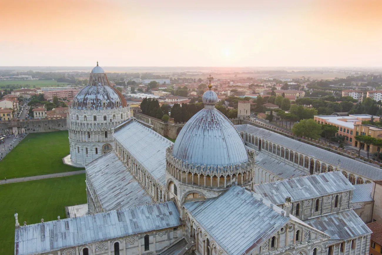 Aerial view over the Pisa Cathedral, Baptistery and green lawn of the Piazza dei Miracoli at sunrise