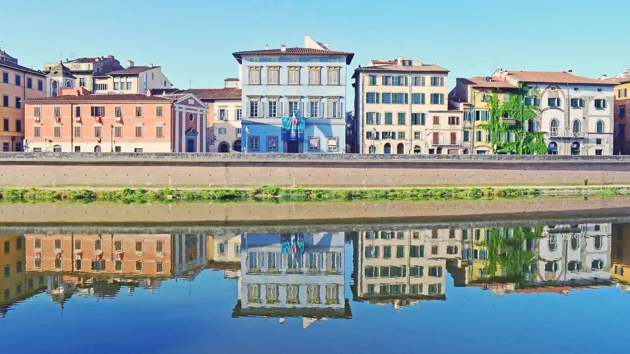 Colourful Lungarno palazzi reflected in the Arno river in Pisa