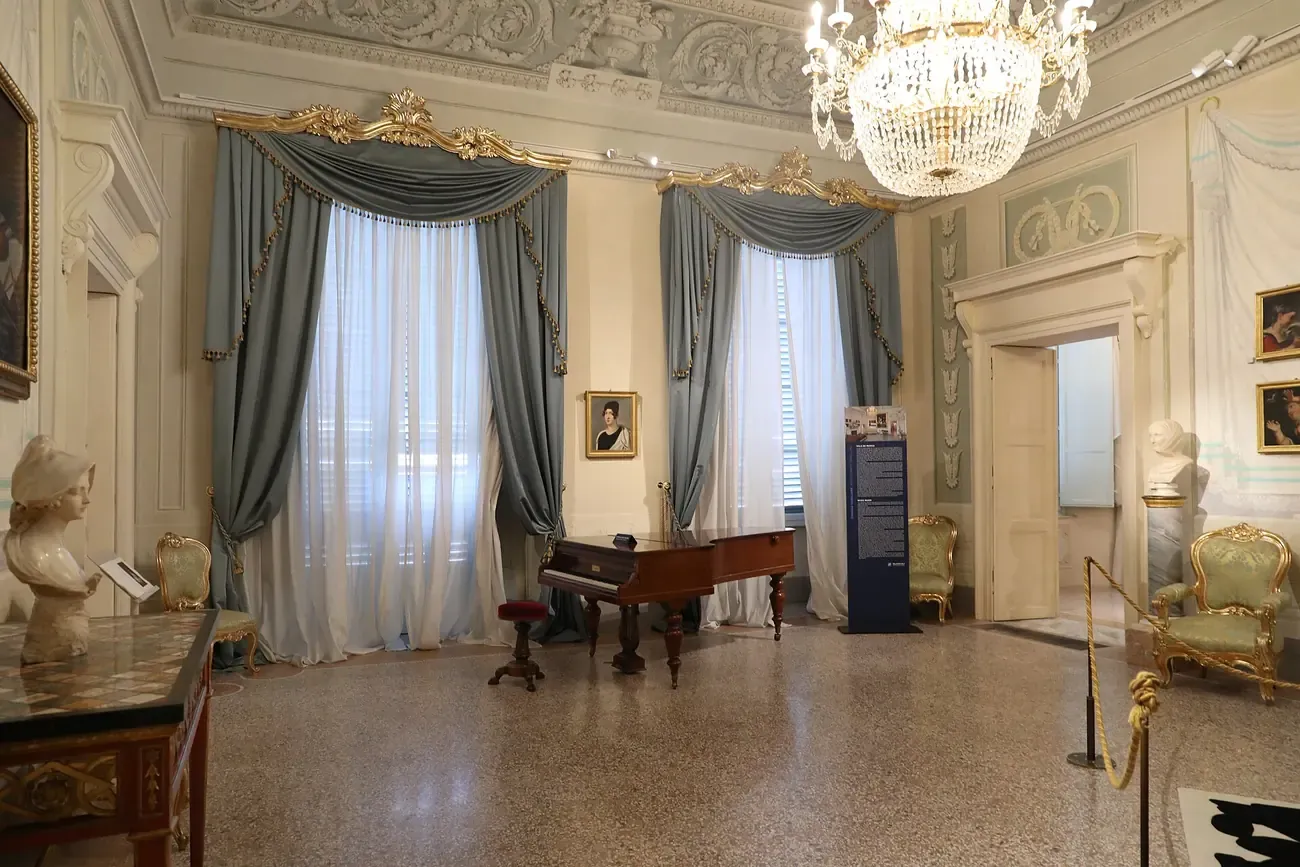 The period music room with chandelier and piano inside Palazzo Blu in Pisa
