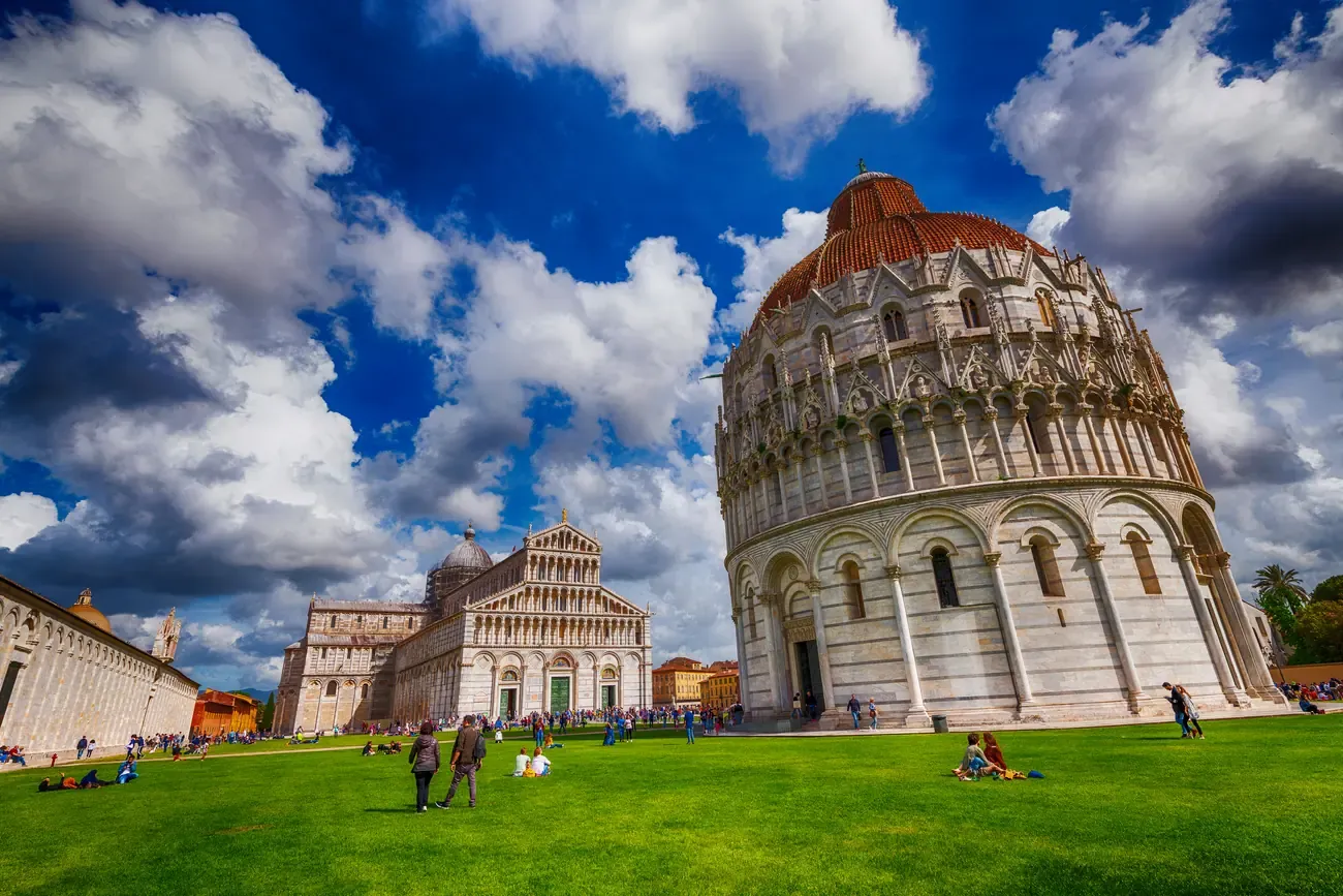 Tourists relaxing on the lawn of the Piazza dei Miracoli in front of the Leaning Tower of Pisa