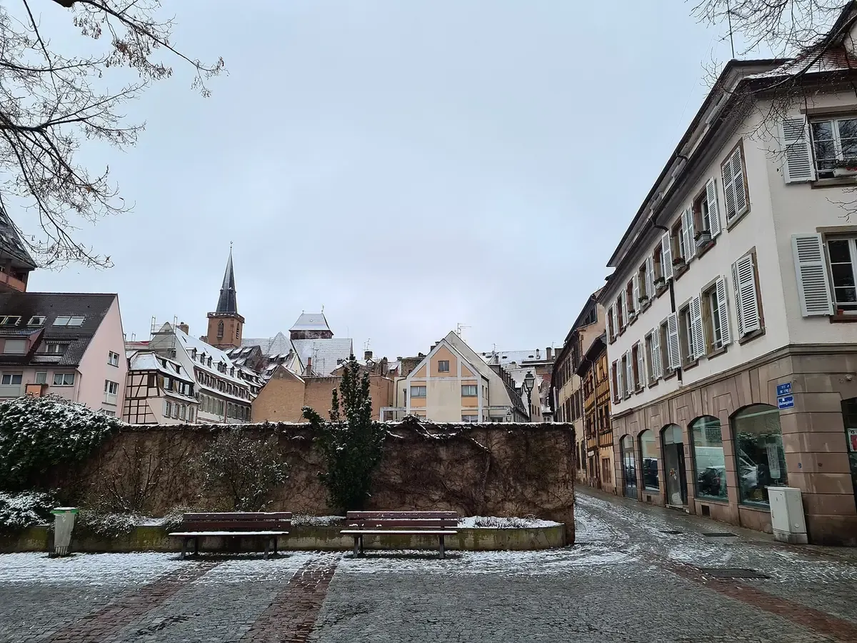 Place Grimmeissen and rue du Coq in Strasbourg under light snow, with a church spire behind