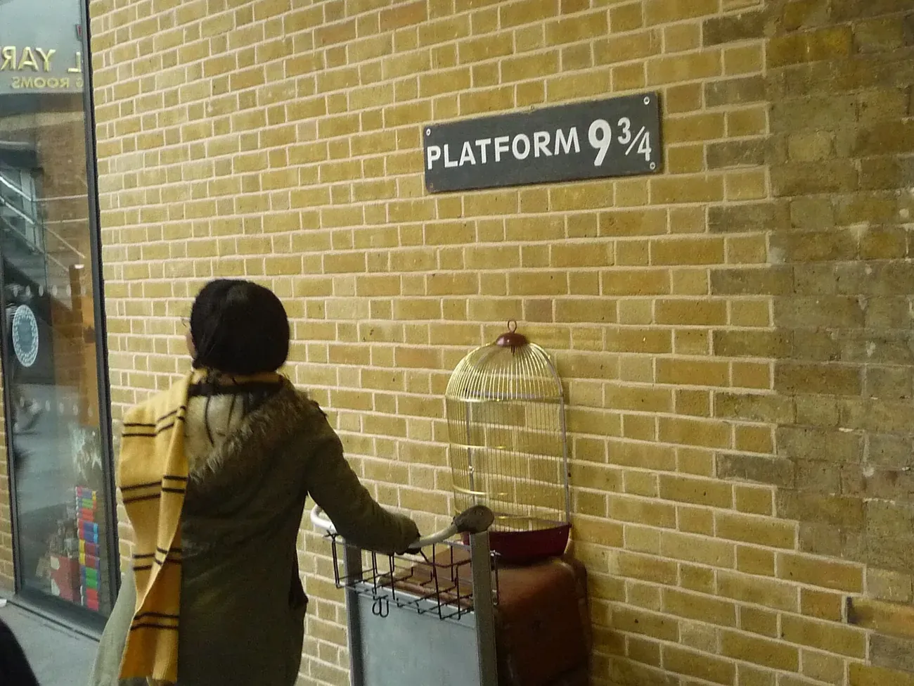 The Platform 9 3/4 sign and luggage trolley half-disappearing into the brick wall at King's Cross station in London