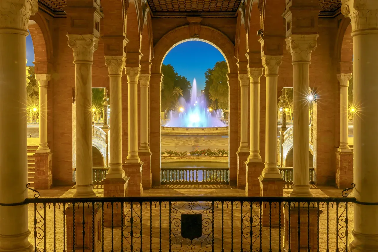 The fountain of Plaza de Espana seen through arches at night, Seville