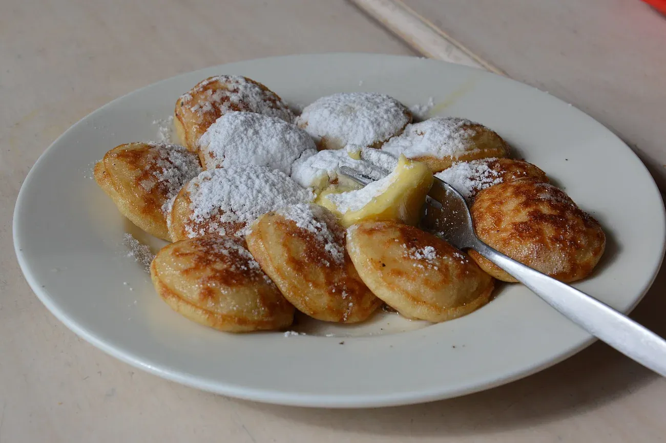 A plate of poffertjes topped with a knob of butter and icing sugar