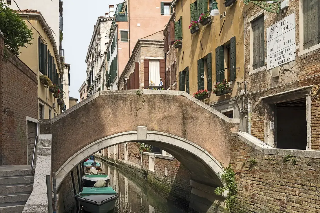 The small stone Ponte delle Tette arching over a narrow canal in San Polo, Venice, with its street sign on the wall