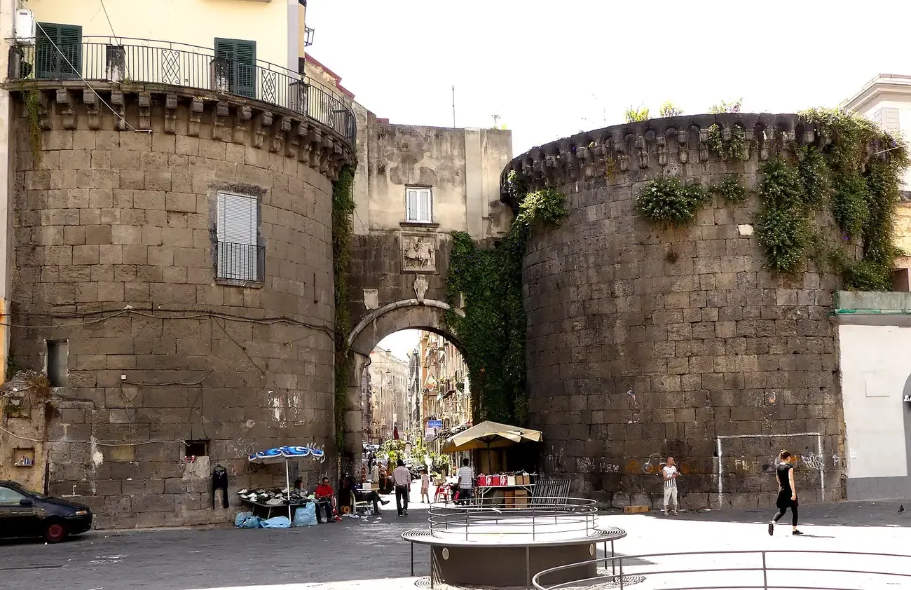 The two round stone towers and the arched gate of Porta Nolana in Naples with market stalls beneath