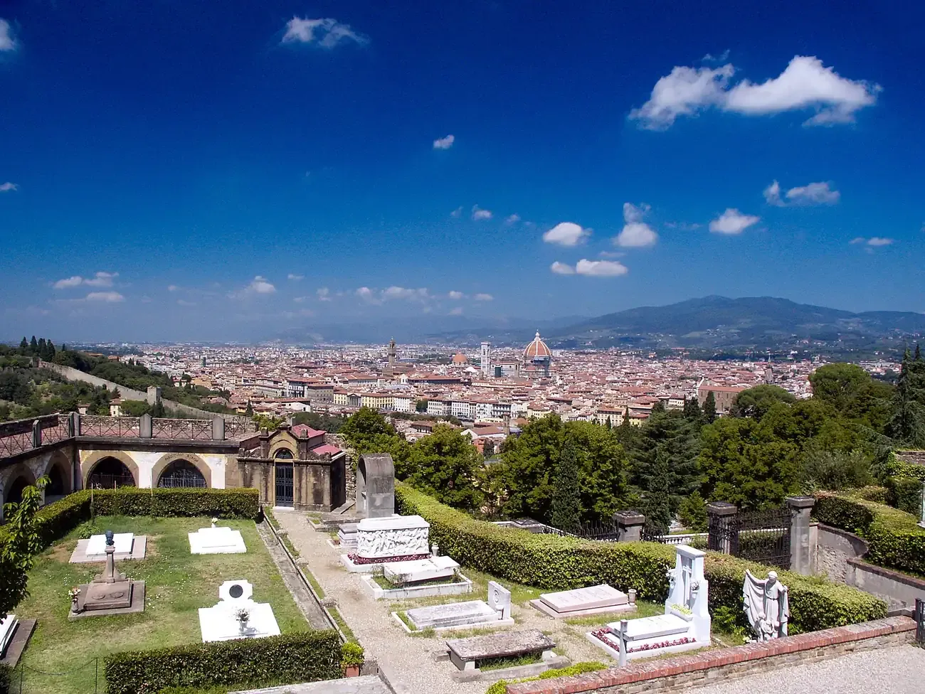 White tombs on the terraced Porte Sante cemetery with the rooftops and dome of Florence in the distance