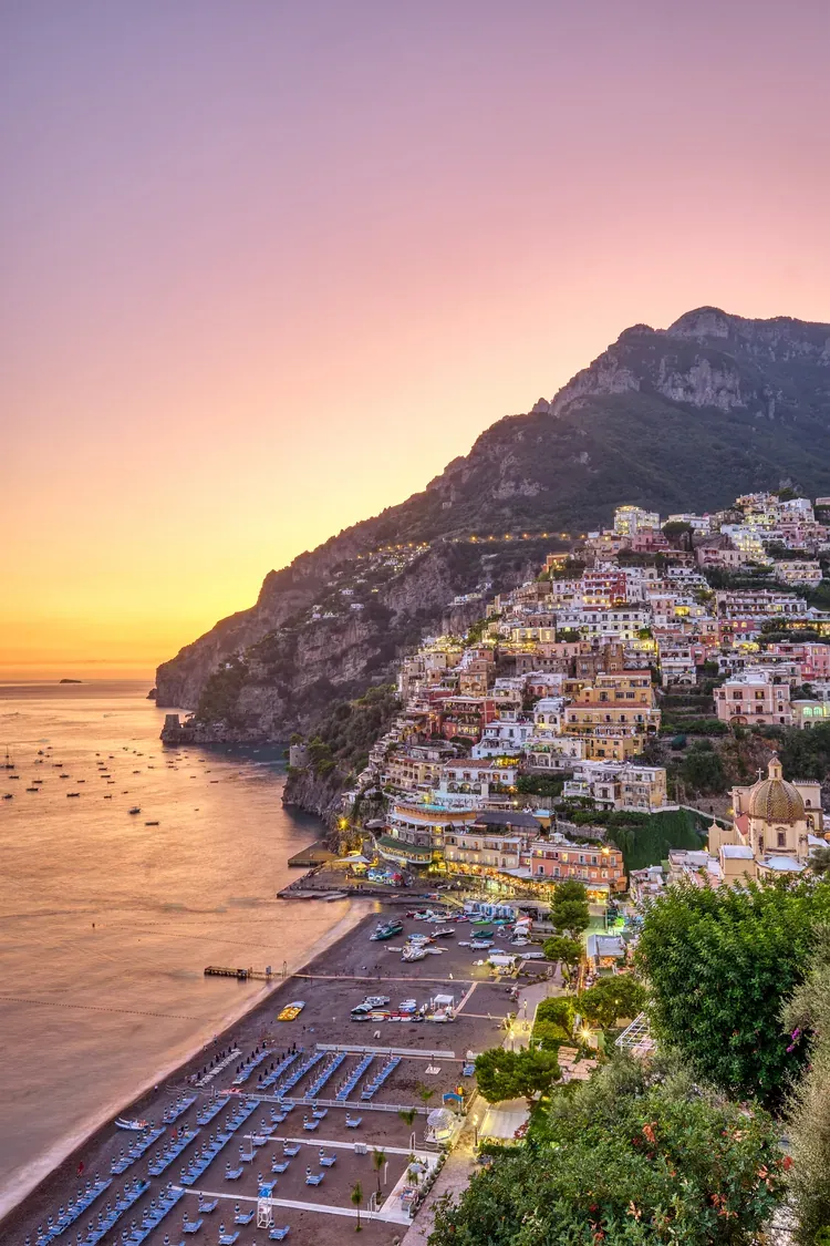 Positano's cliffside houses lit up at dusk above the beach on the Amalfi Coast