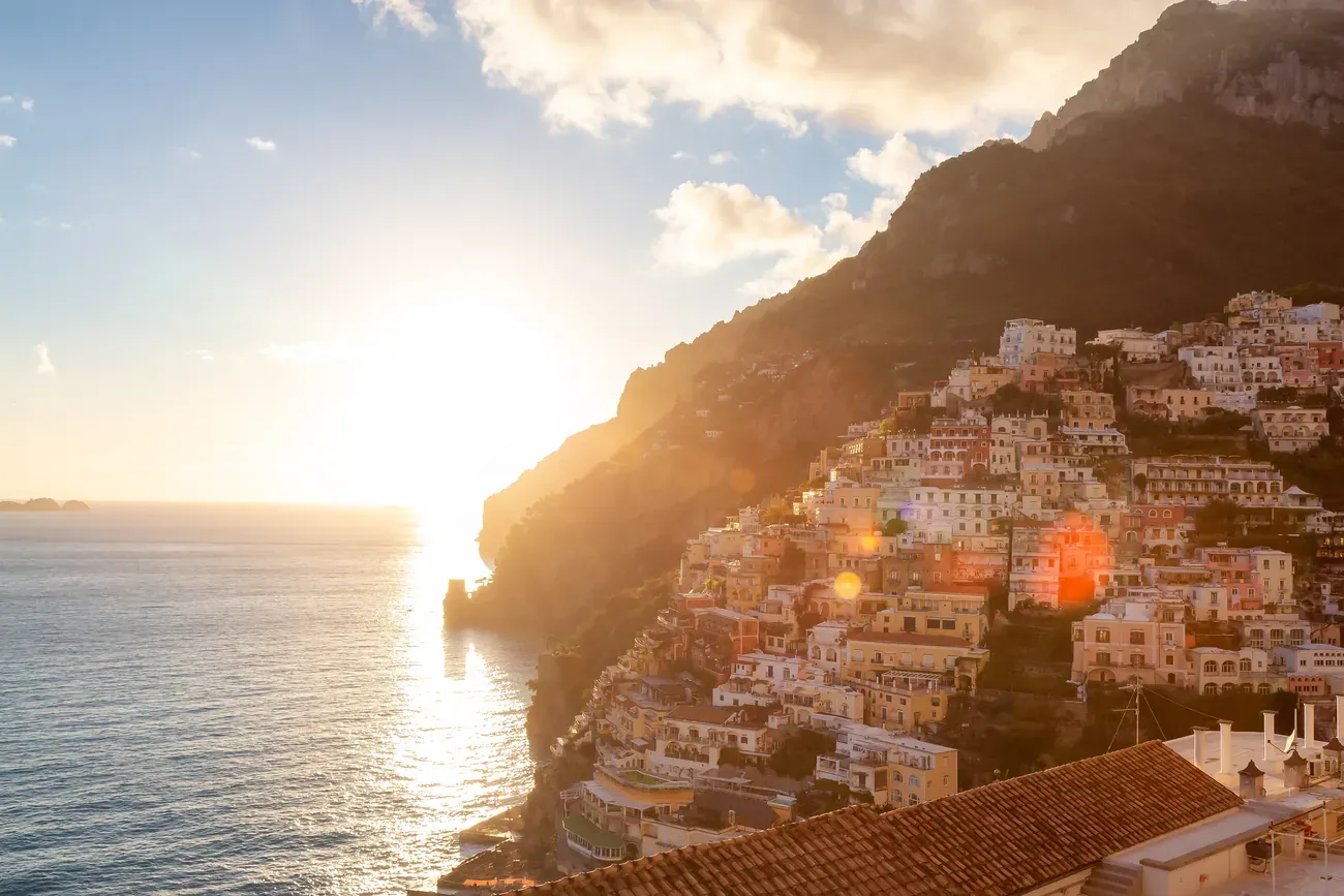 Positano seen from a terrace at sunset, with the sun setting over the sea