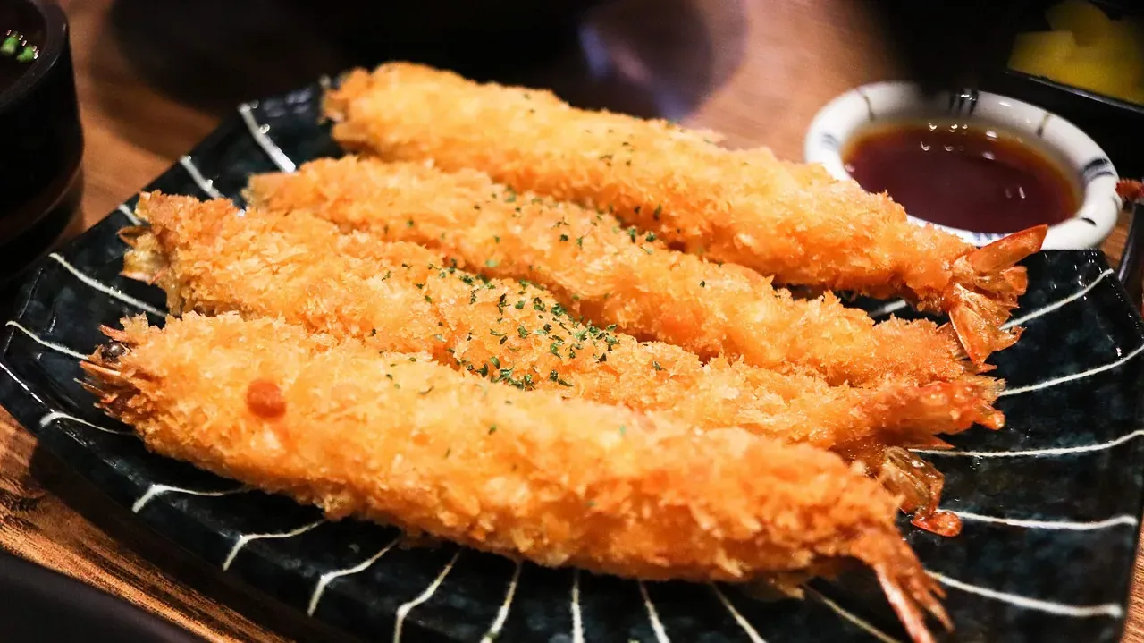Prawn tempura on a black plate with a bowl of dipping sauce