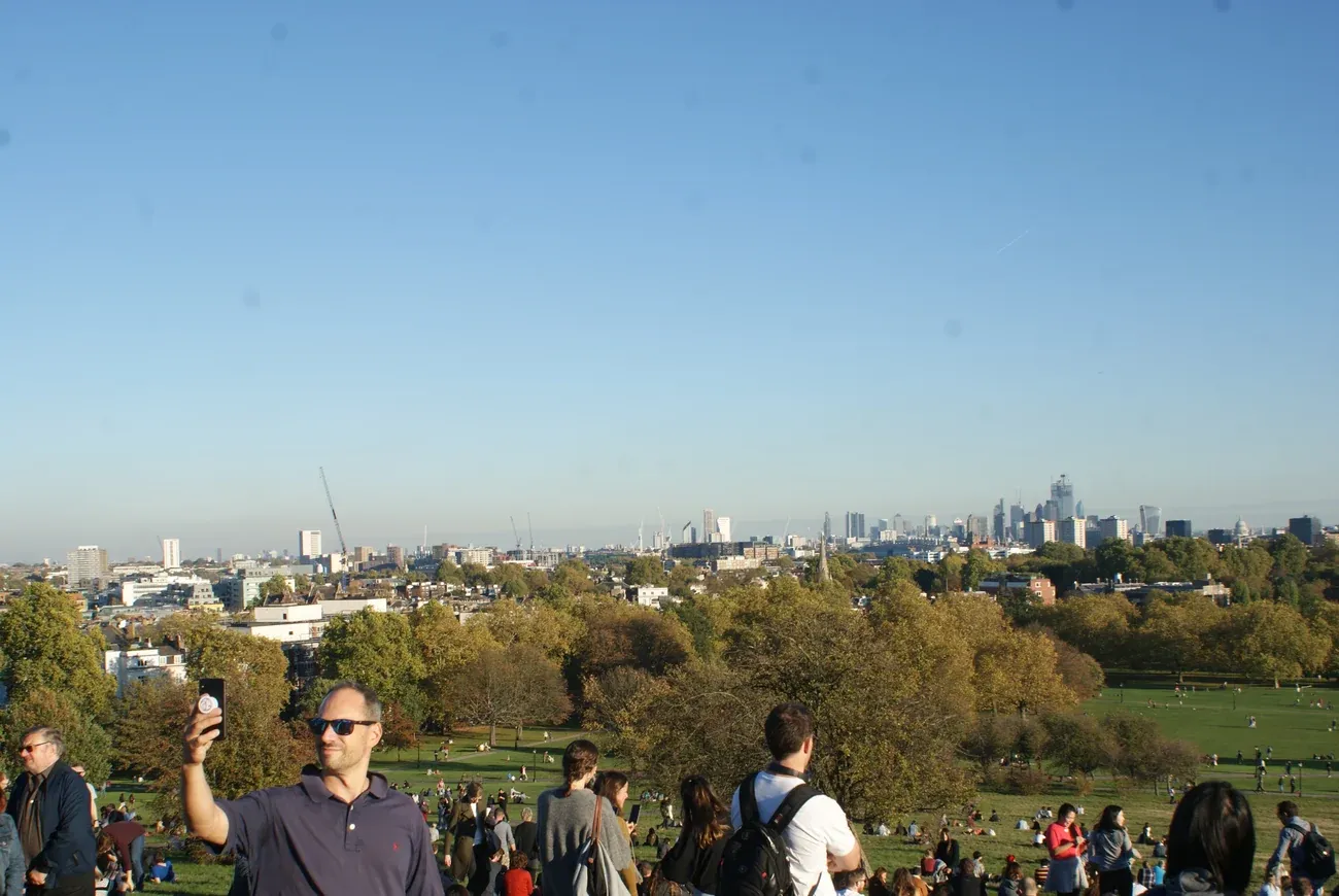 Visitors on the summit of Primrose Hill looking south over the trees to the central London skyline