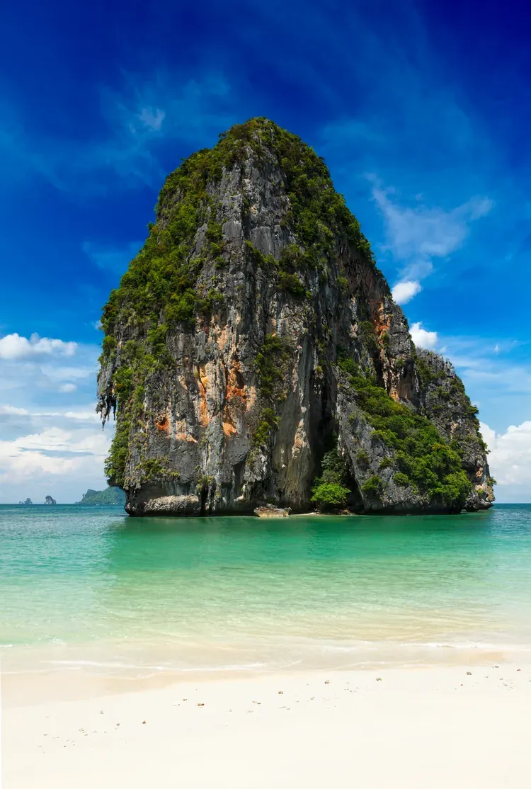 A towering limestone cliff over the white sand of Railay Beach, Krabi