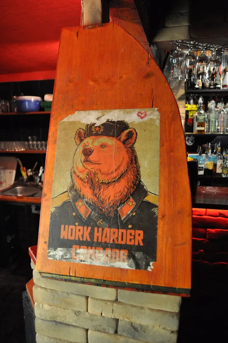 A Soviet-style Work Harder Comrade bear poster on the wooden bar post inside the Red Ruin bar in Budapest