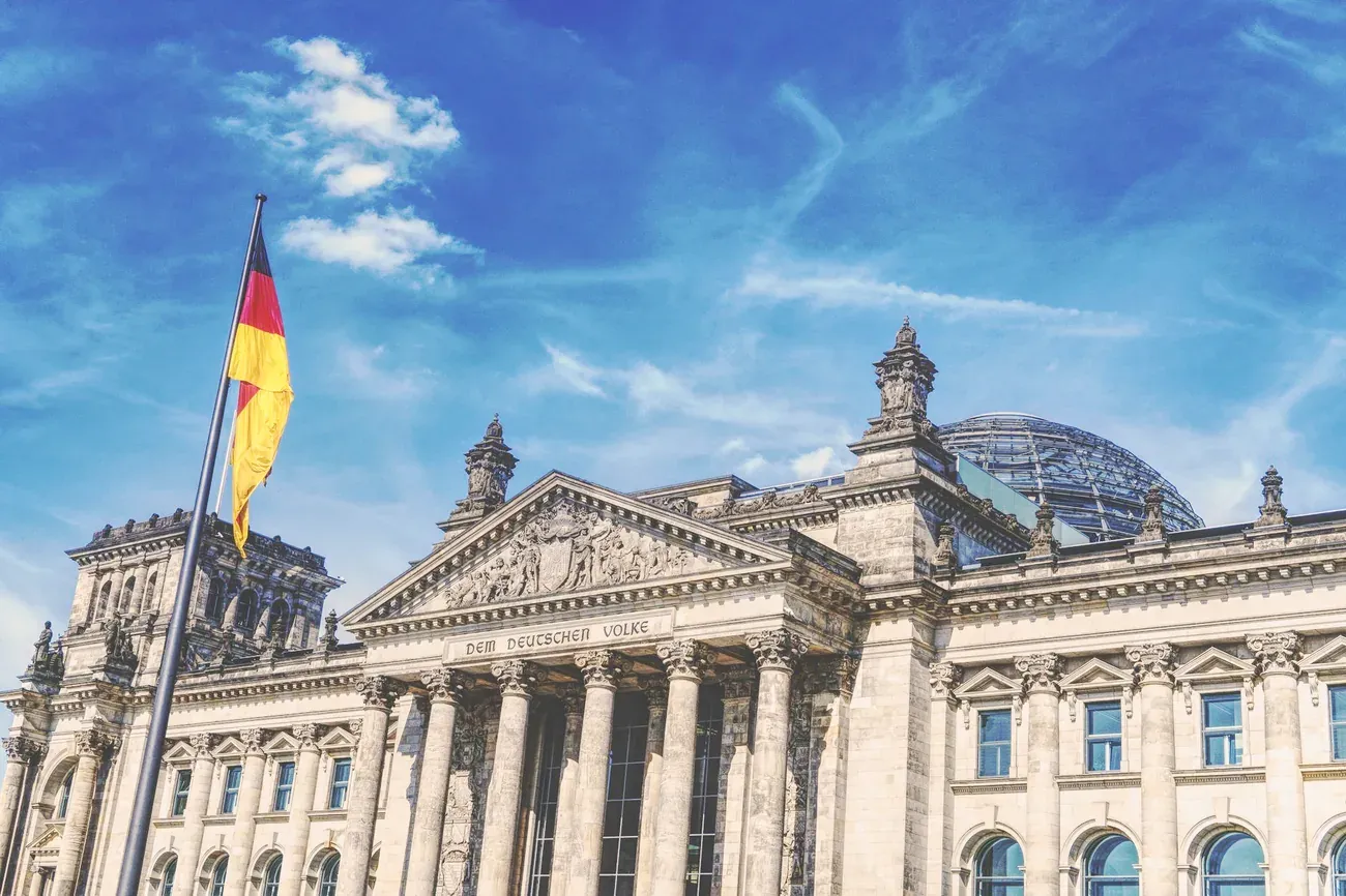The Reichstag building in Berlin under a blue sky with the German flag