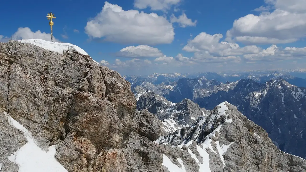 The rocky summit of the Zugspitze with its golden cross and the Alps beyond