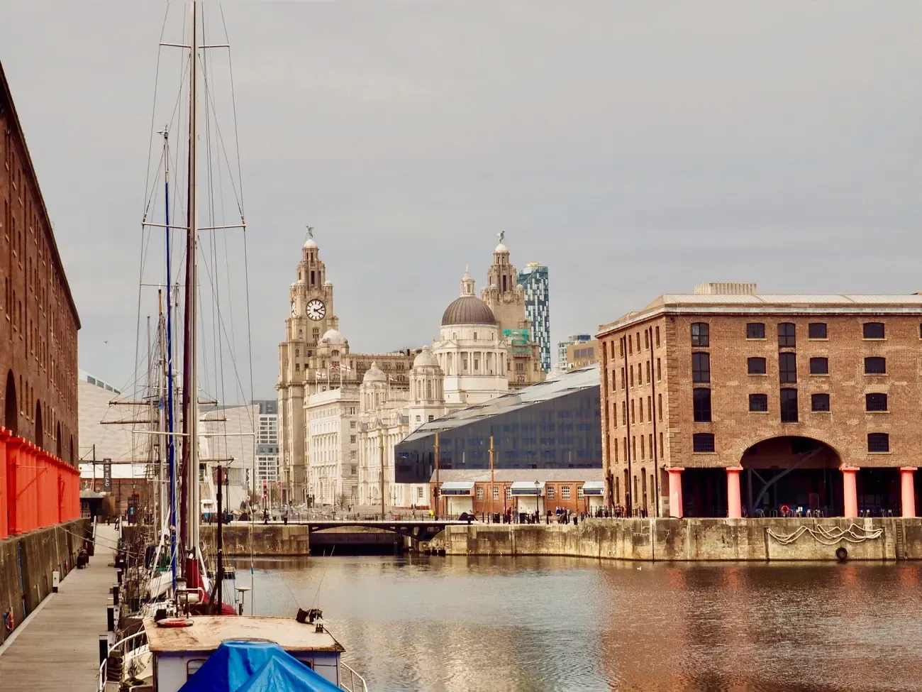 Brick warehouses and moored boats at the Royal Albert Dock with the Royal Liver Building and the Three Graces behind in Liverpool