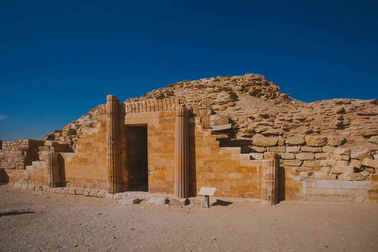 Ancient ruined stone tombs in the Saqqara necropolis under a blue sky, near Cairo.