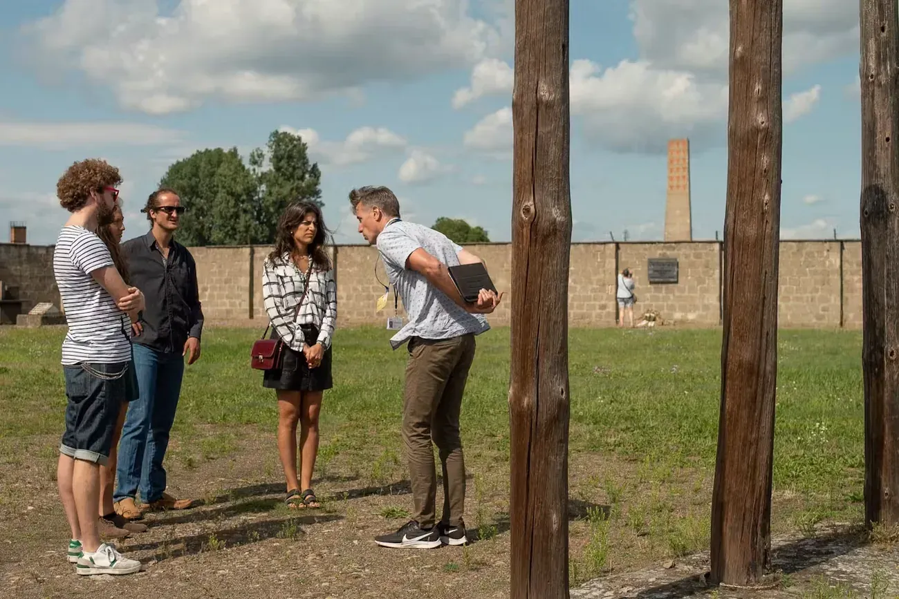 A guide briefing a group at Sachsenhausen Memorial, with the memorial tower in view
