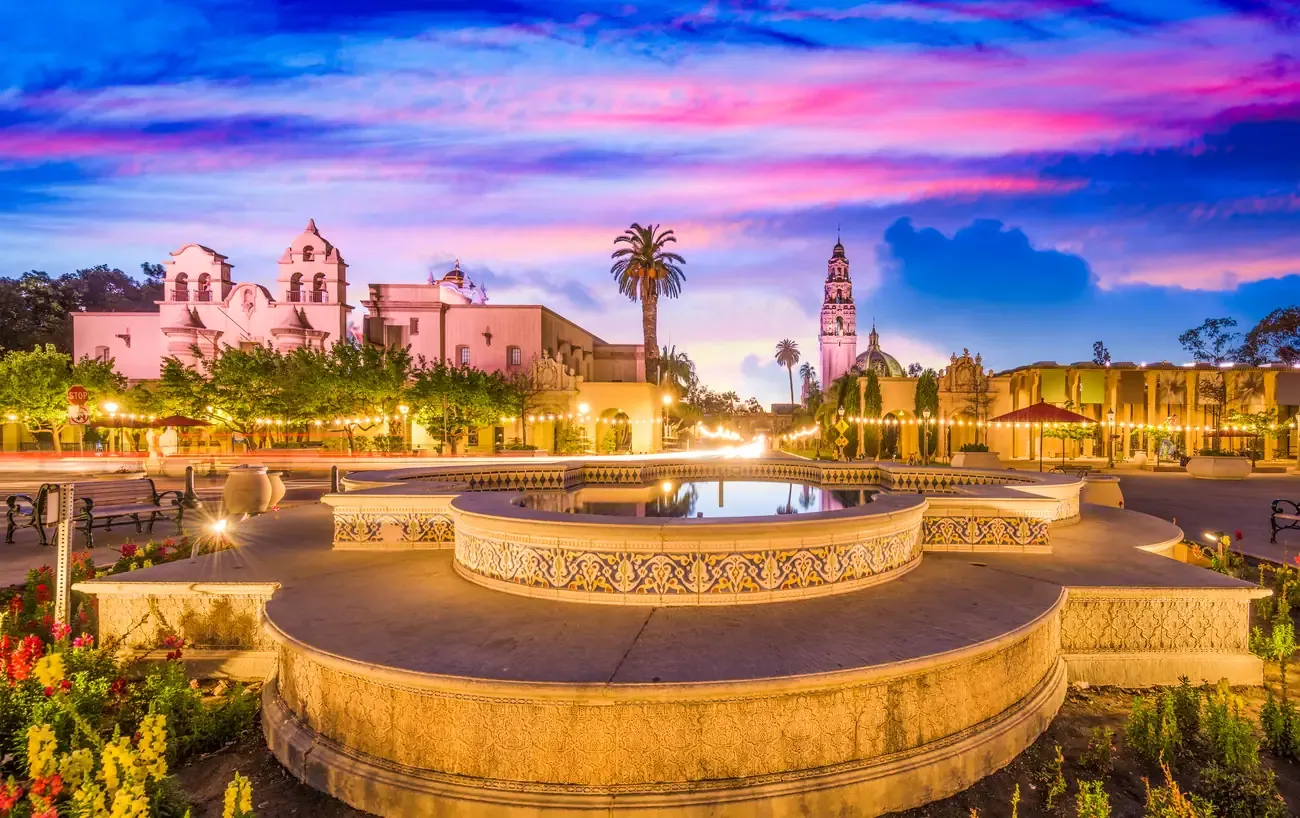 Fountain and Spanish colonial buildings of Balboa Park under a pink sunset sky in San Diego