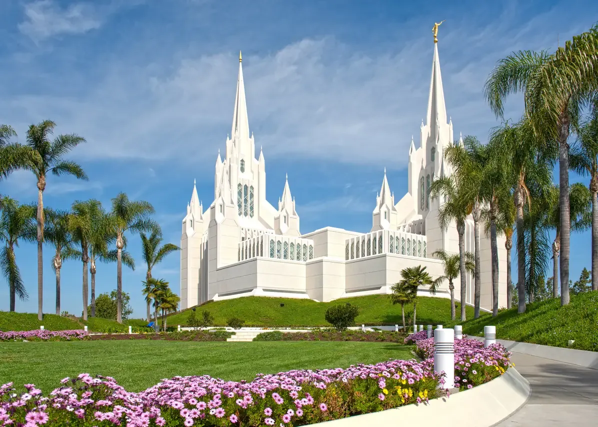 White marble spires of the San Diego California Temple rising above palm trees and flowerbeds