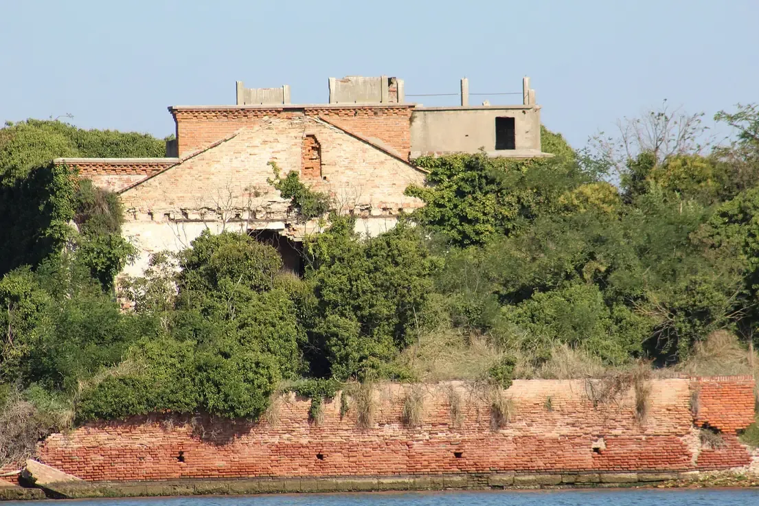 The crumbling brick walls and overgrown ruins of the abandoned island of San Giorgio in Alga seen from the water