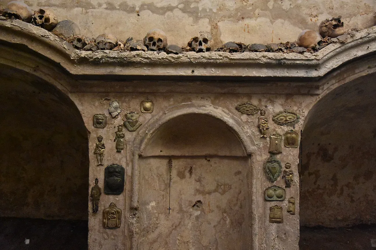 Skulls on a ledge above an altar niche covered with votive plaques in the Church of Santa Luciella ai Librai in Naples