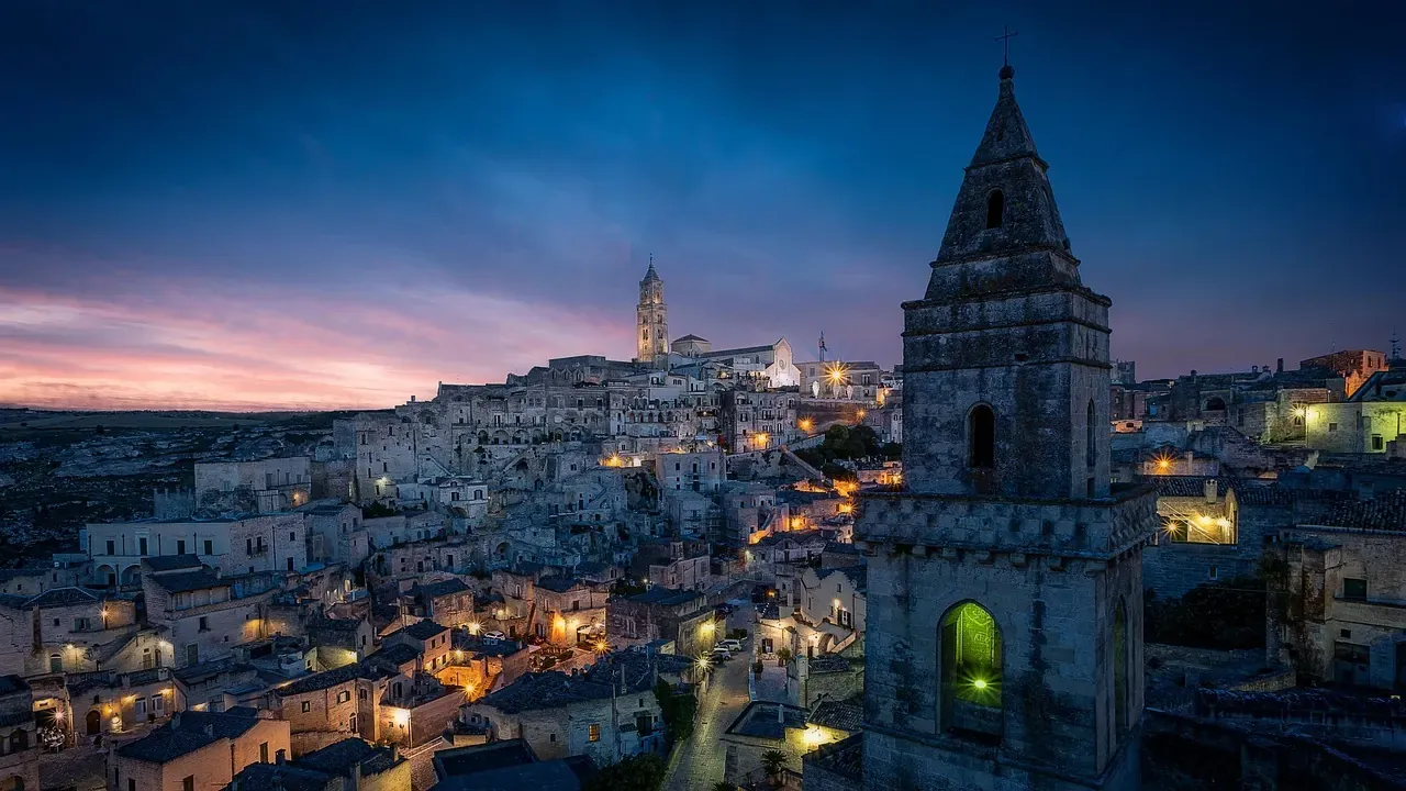 The cave dwellings of the Sassi di Matera and the bell tower of San Pietro Barisano at dusk in Matera, Basilicata
