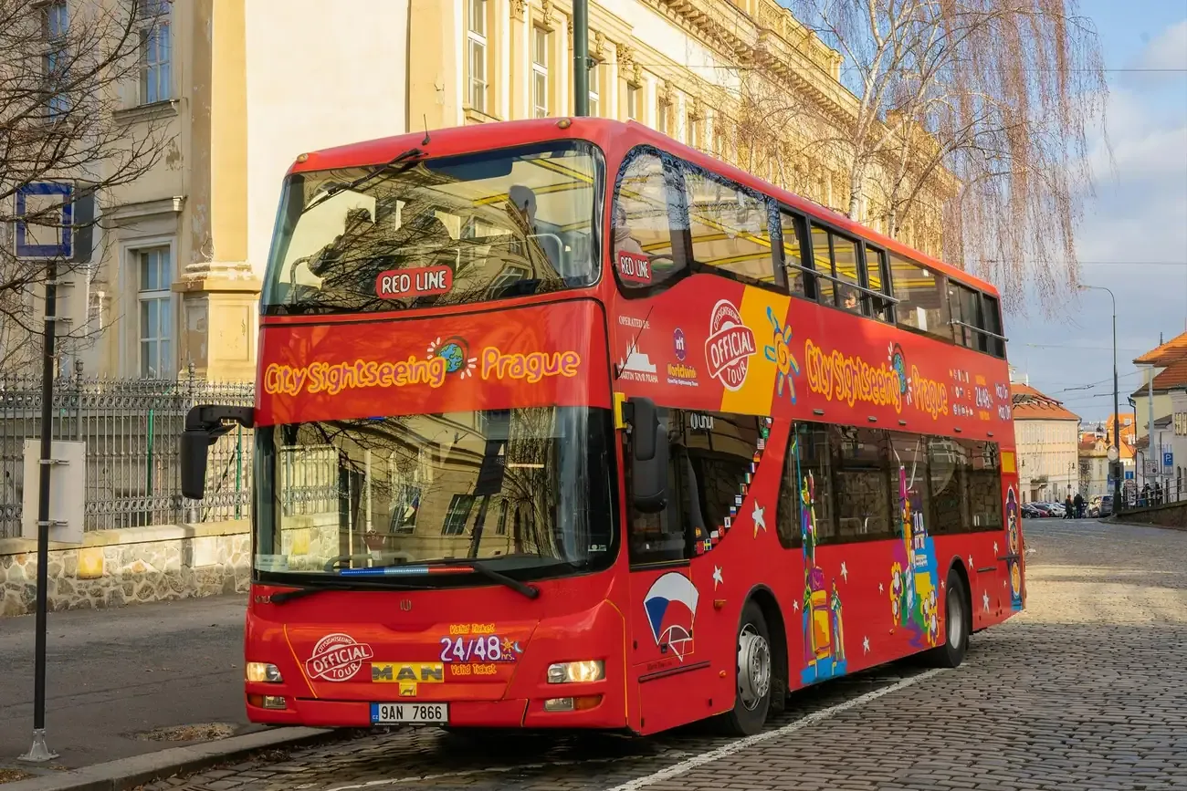 A red open-top sightseeing bus on a street in Prague