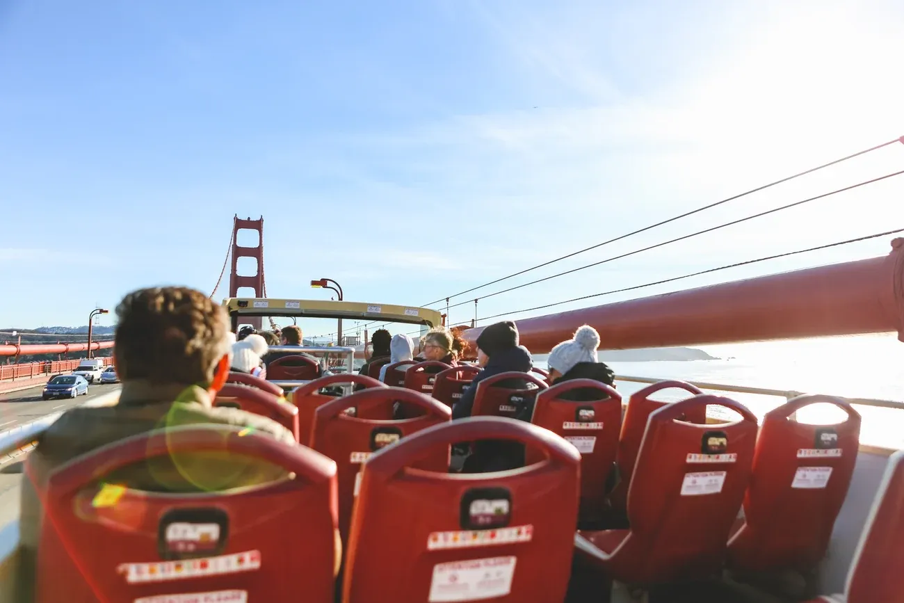 Passengers on the top deck of an open-top sightseeing bus crossing the Golden Gate Bridge in San Francisco