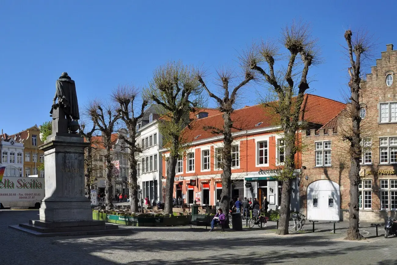 The statue of Simon Stevin on Simon Stevinplein in Bruges, with pollarded trees and gabled houses on a sunny day
