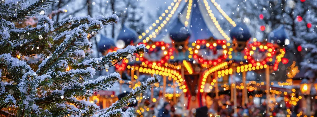 A snow-covered fir tree in front of a lit carousel at Christmas in Tivoli Gardens, Copenhagen