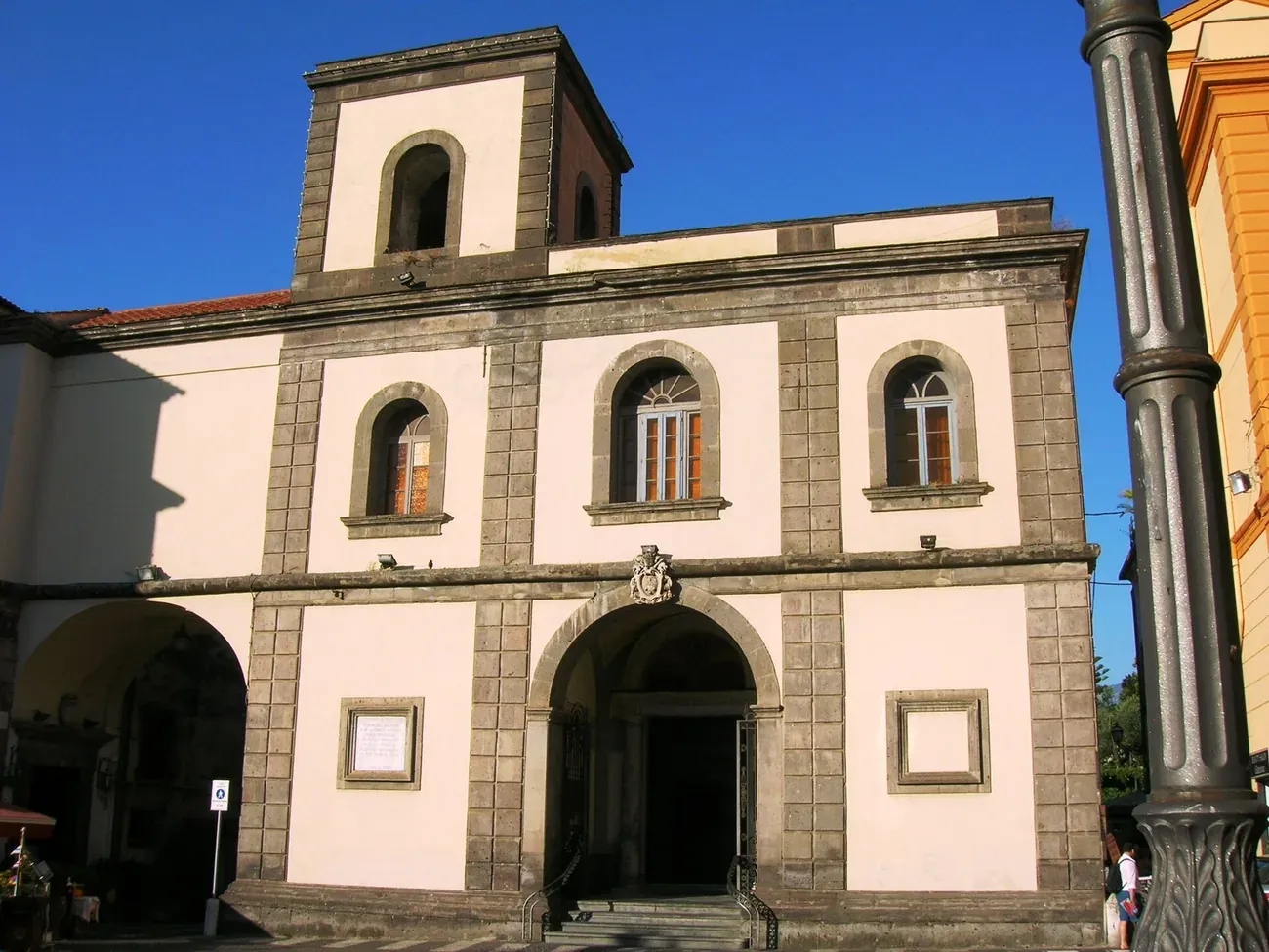 The facade and bell tower of the Basilica di Sant'Antonino in Sorrento under a clear blue sky