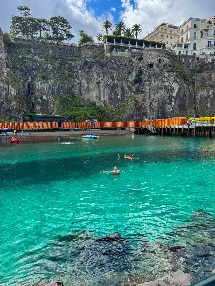 Swimmers in the turquoise waters of a cove beneath Sorrento's cliffs