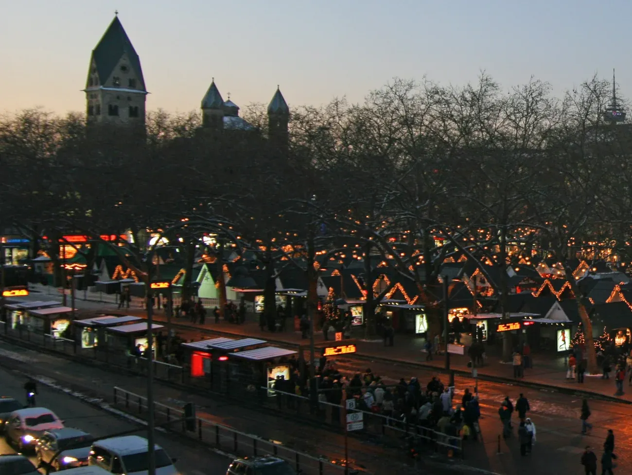 The towers of St. Aposteln above Christmas market stalls on Neumarkt at dusk, Cologne