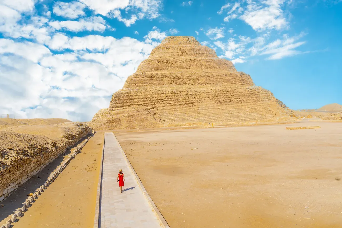 The Step Pyramid of Djoser at Saqqara with a visitor in a red dress walking along the causeway, near Cairo.