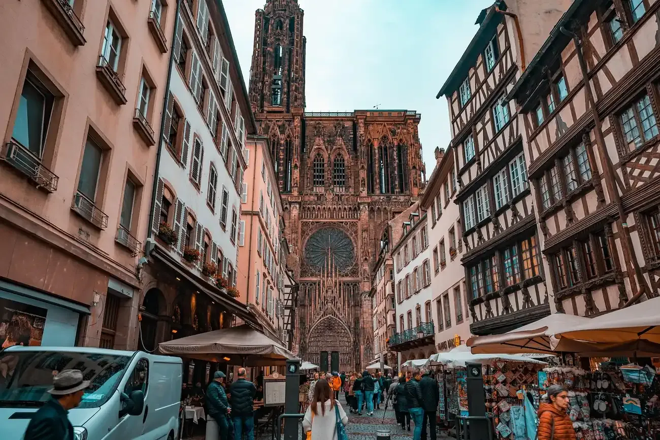 The pink sandstone facade and spire of Strasbourg Cathedral seen from a street of half-timbered houses