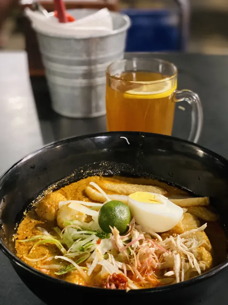 A bowl of laksa noodles served with lemon tea, a Kuala Lumpur specialty.