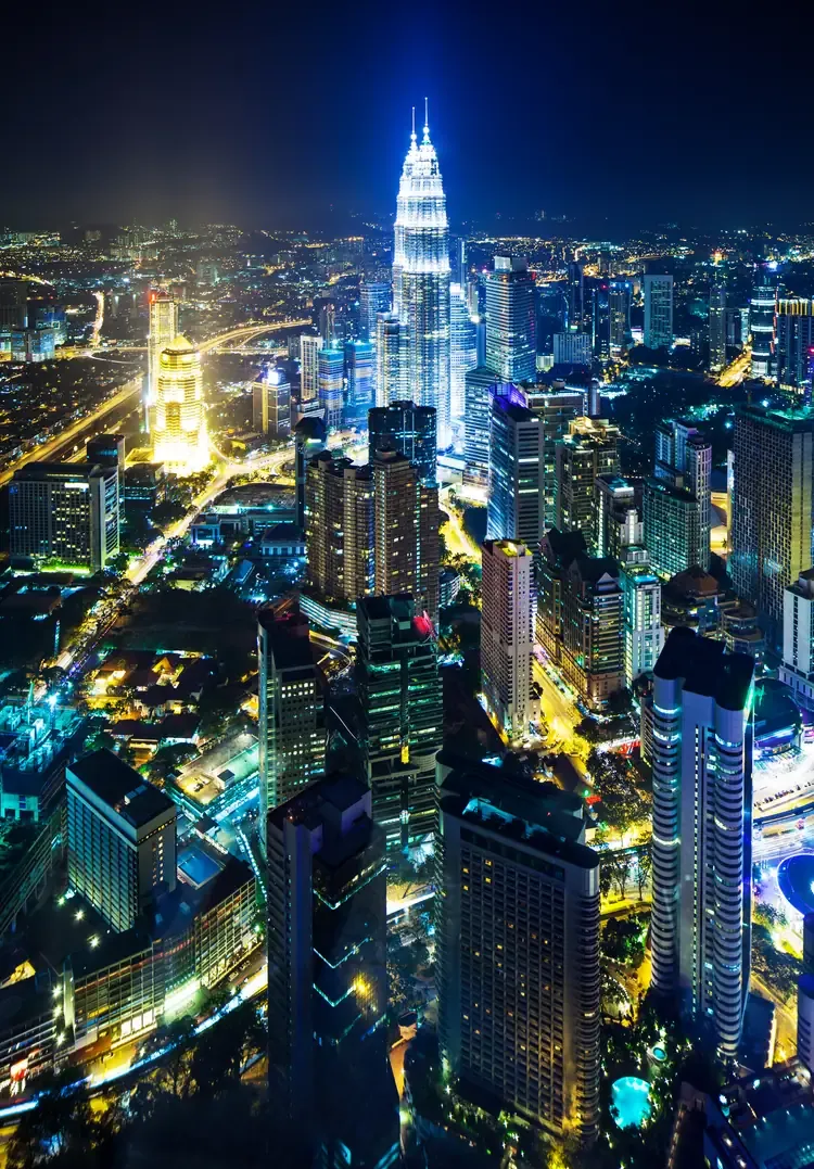 The Petronas Twin Towers illuminated above the Kuala Lumpur skyline at night.