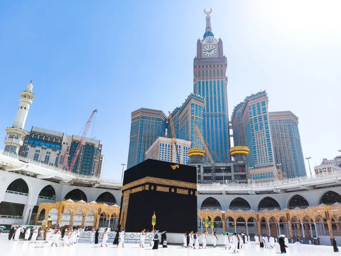 Pilgrims walking around the Kaaba courtyard in bright daylight.