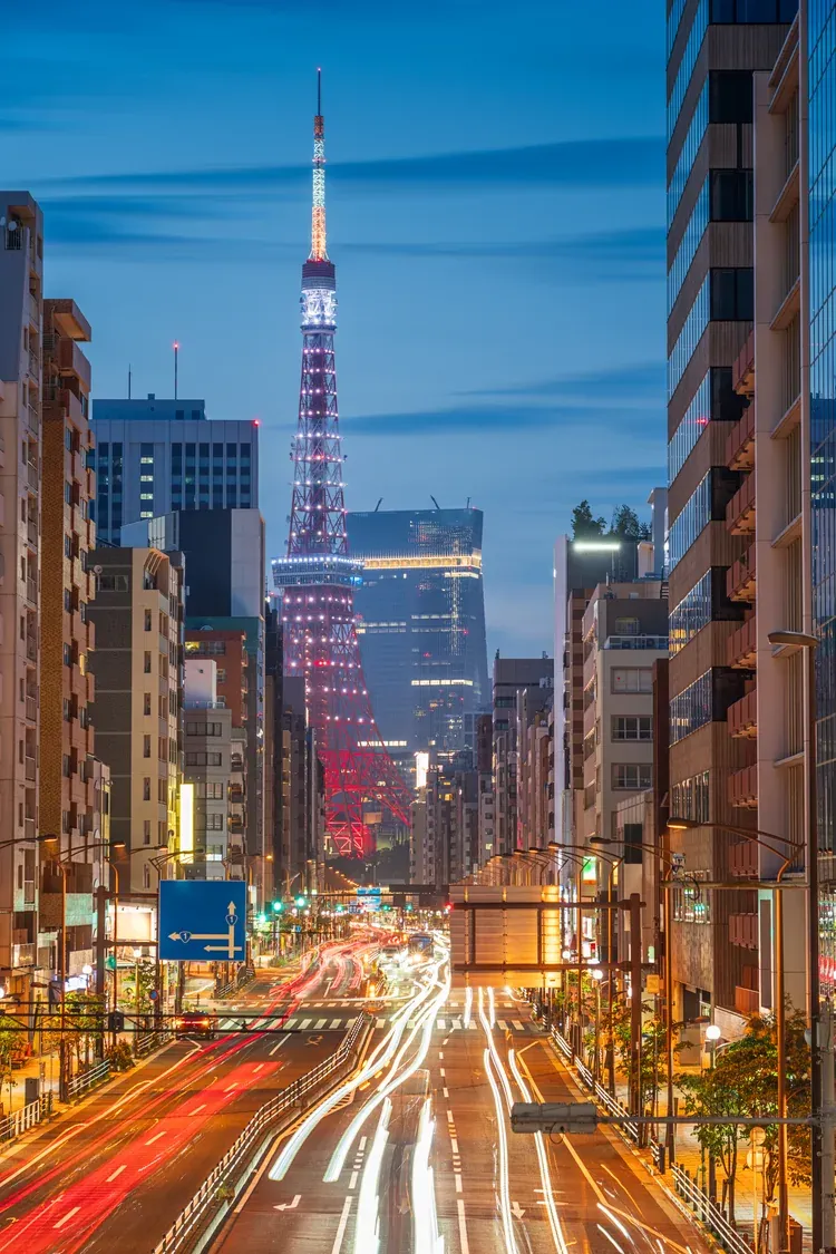 Tokyo Tower rising at the end of a busy street with light trails at night