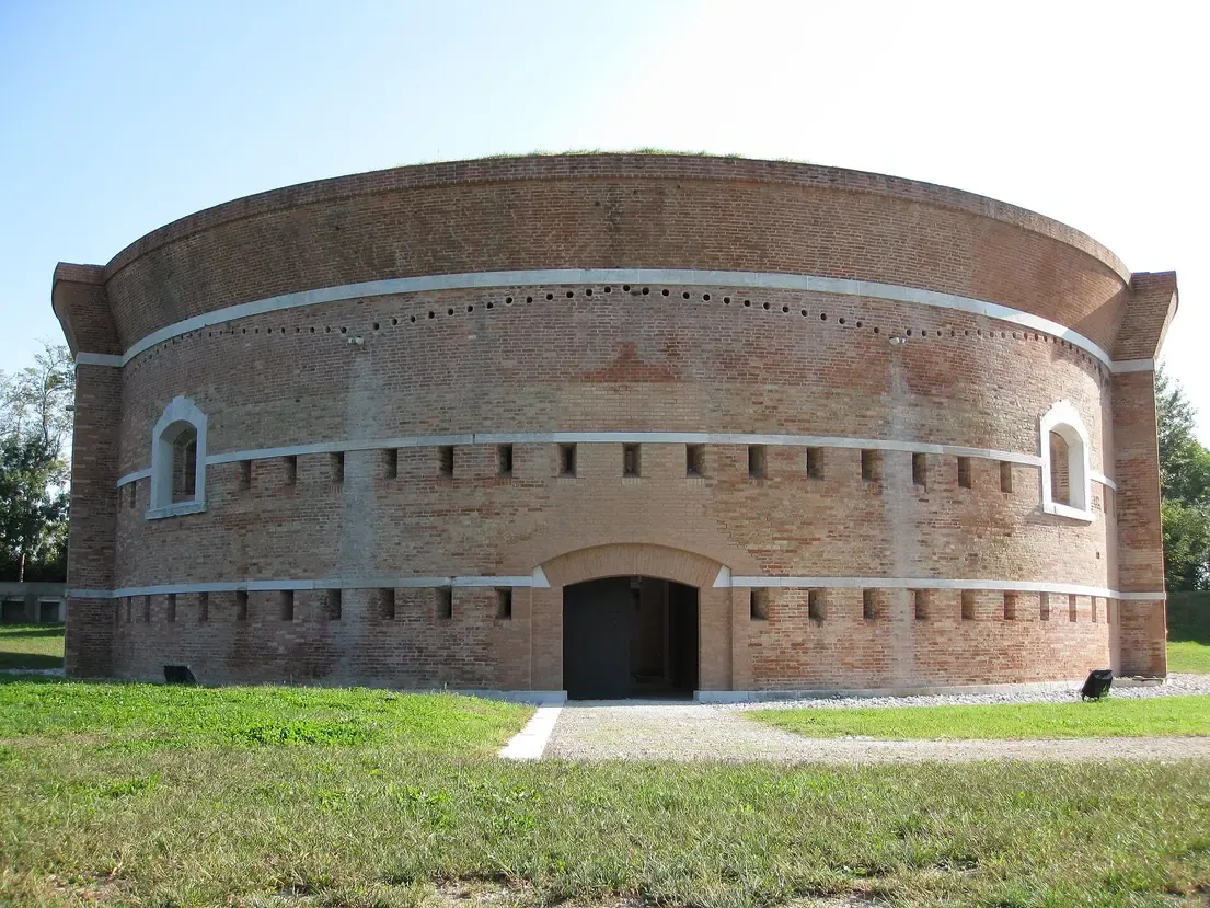 The round brick Torre Massimiliana gun tower with its entrance on the grass of Sant'Erasmo island in the Venetian lagoon