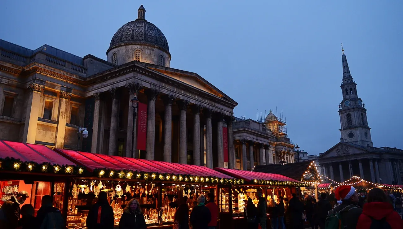 Trafalgar Square Christmas Market stalls at dusk, with the National Gallery and St Martin-in-the-Fields behind