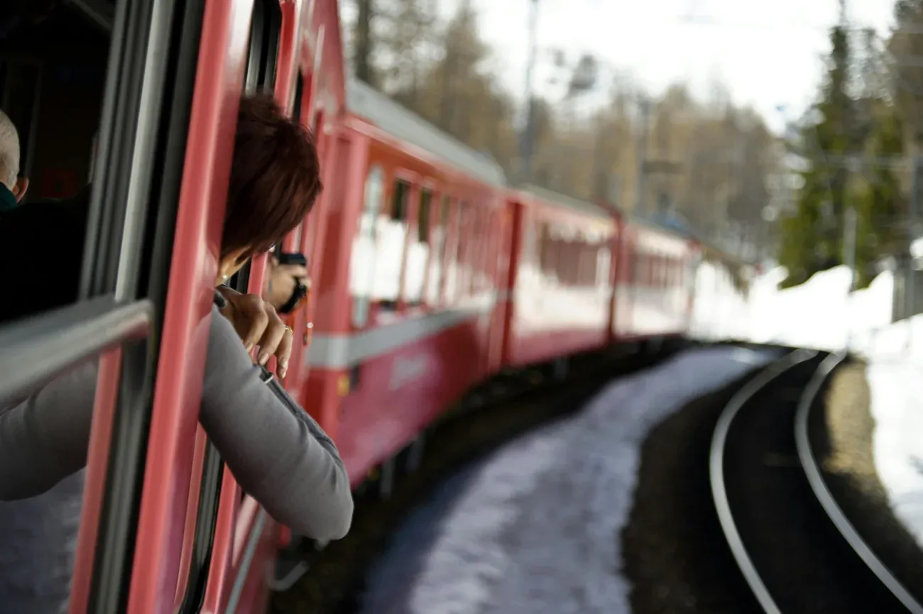 Traveller leaning out of an open window of the red Bernina train to take a photo of the snowy track