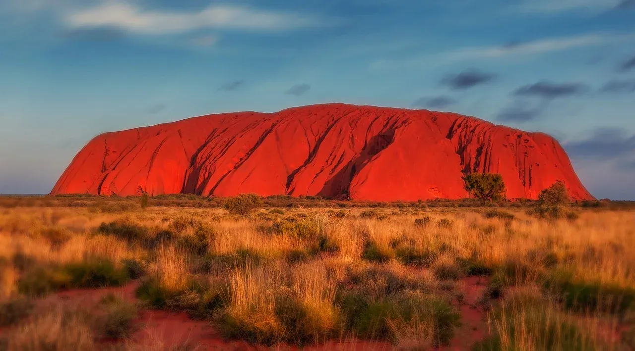 Uluru glowing red above the spinifex plain at sunset in the Northern Territory