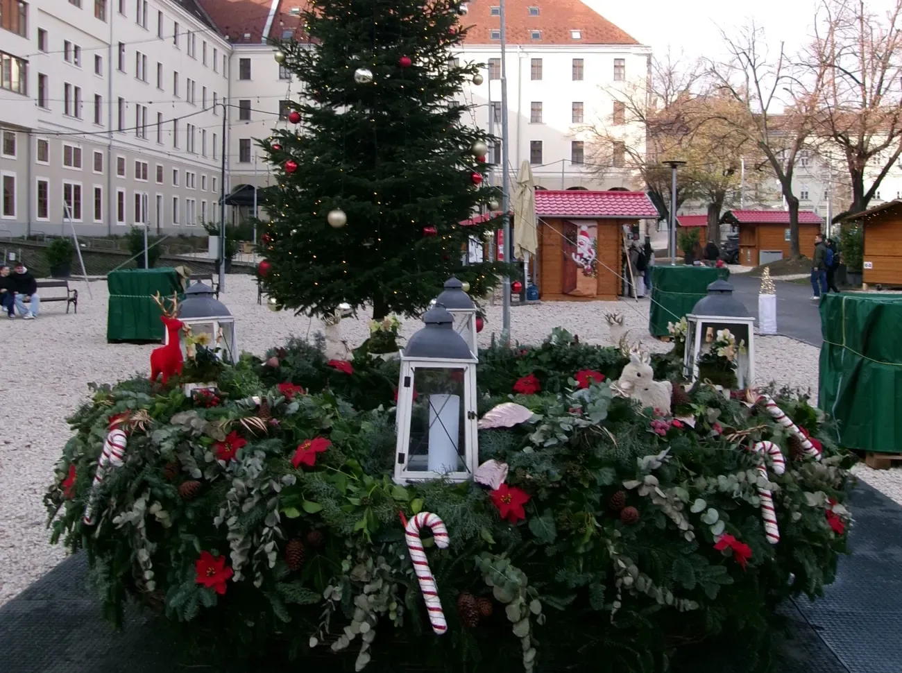 An Advent wreath with candles and a Christmas tree in Városháza Park in Budapest, with market stalls behind