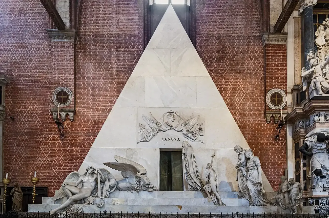 The white marble pyramid tomb of Antonio Canova against the brick wall of the Frari basilica in Venice
