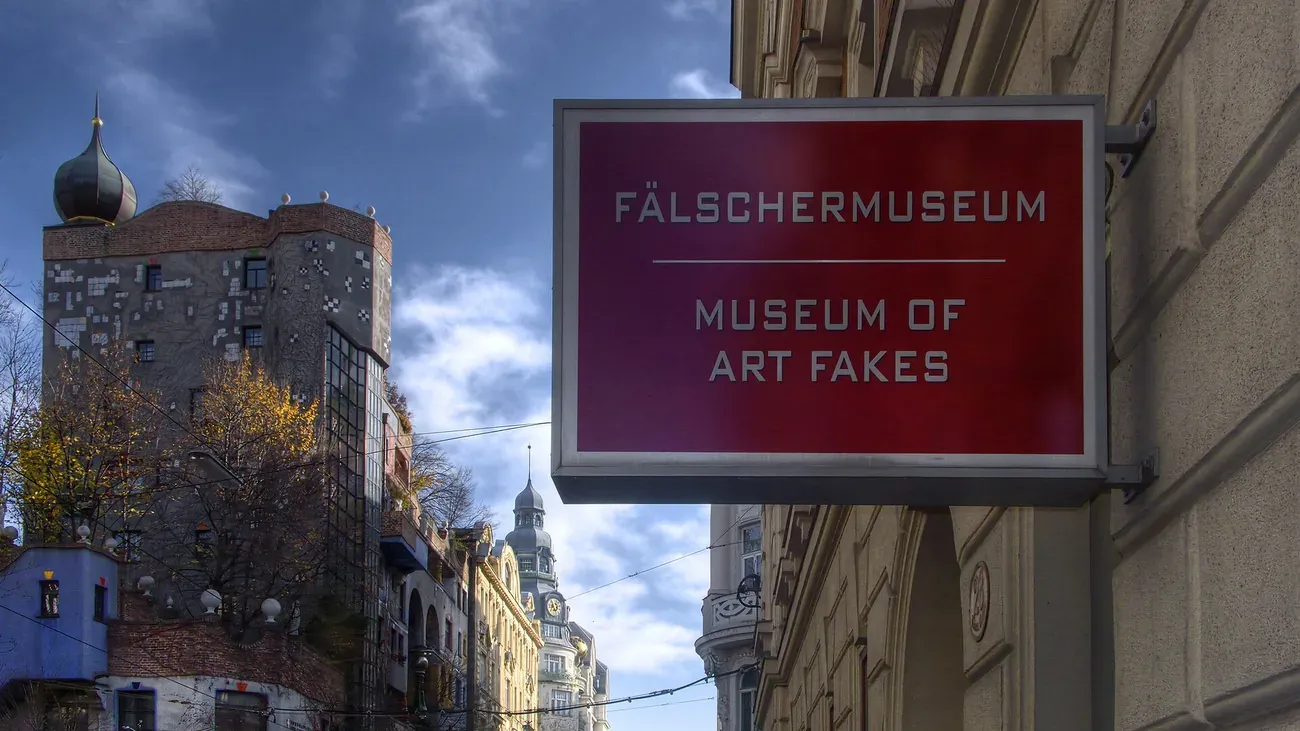 The Fälschermuseum (Museum of Art Fakes) sign mounted on its building facade in Vienna, with the Hundertwasserhaus visible behind