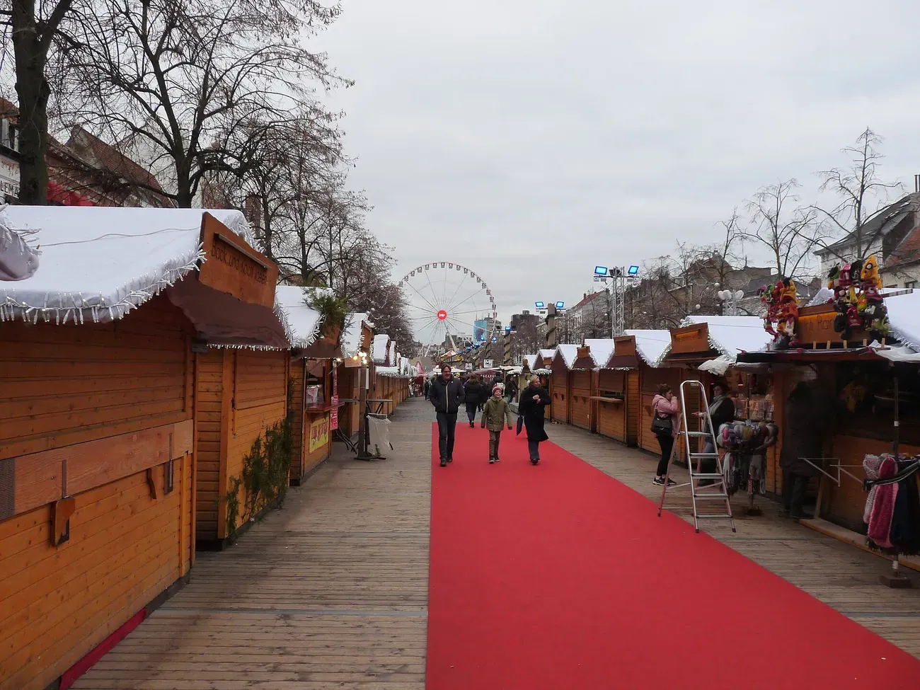 Rows of wooden chalets with snow-effect roofs on the Vismet in Brussels, with the Ferris wheel behind