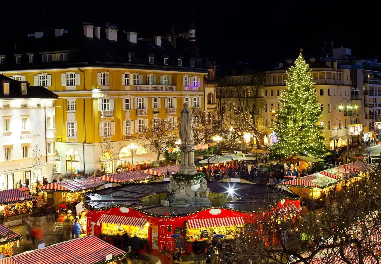 The Walther monument surrounded by Christmas market stalls and a lit Christmas tree on Piazza Walther, Bolzano
