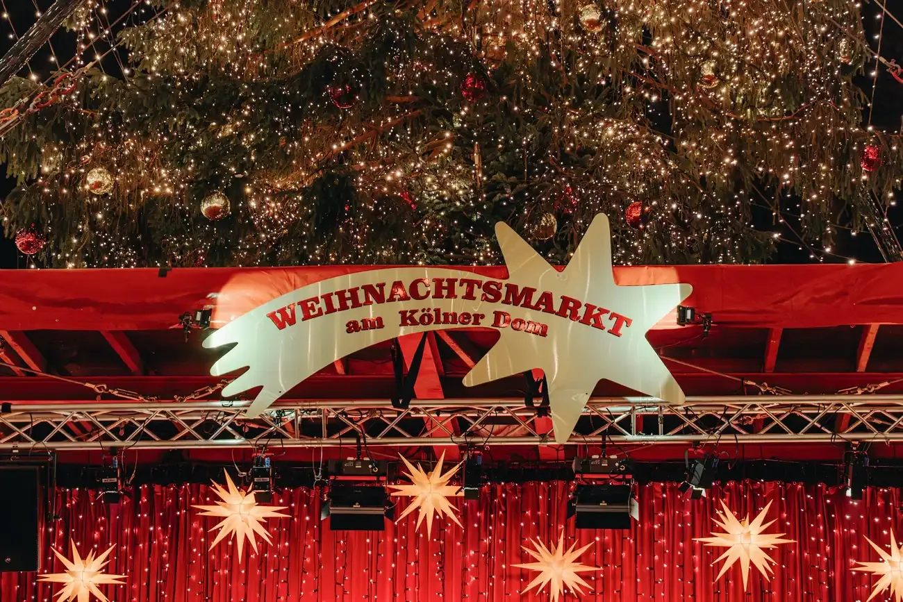 The Weihnachtsmarkt am Kölner Dom sign under the lit Christmas tree at the Christmas market at Cologne Cathedral
